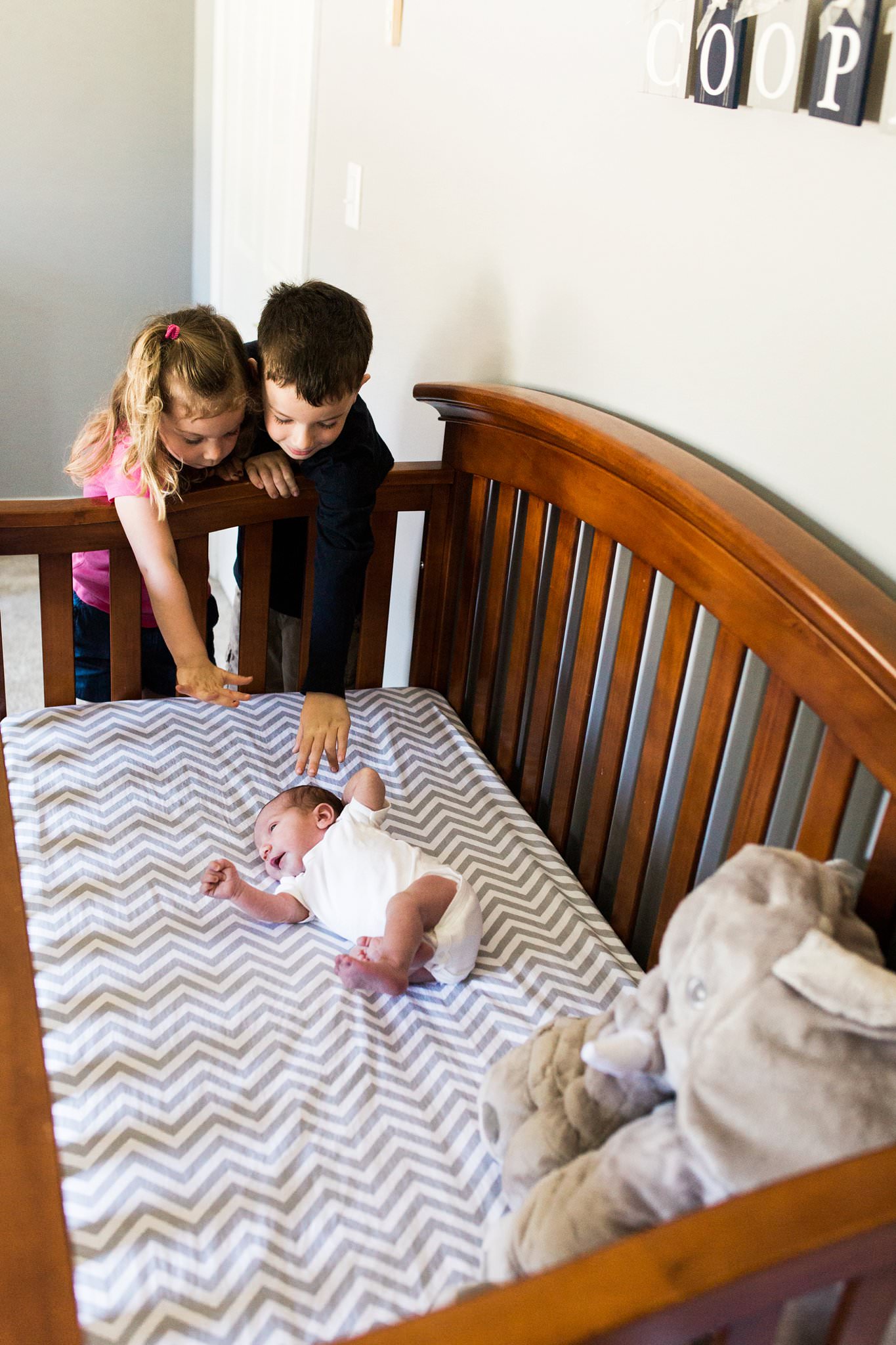 older siblings looking at baby in crib