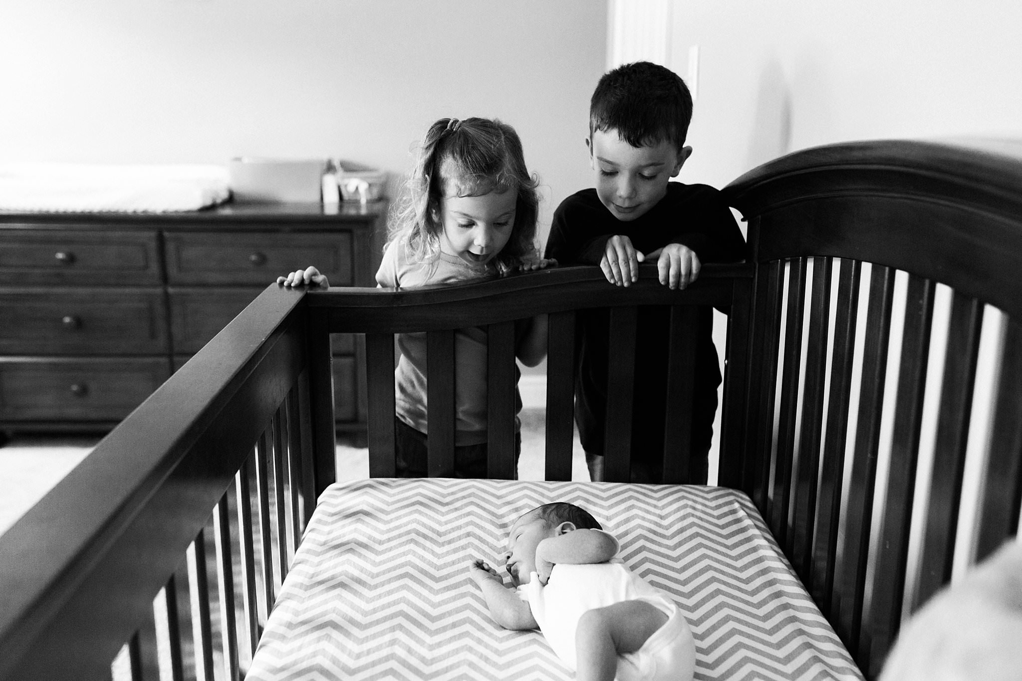 older siblings looking at baby in crib