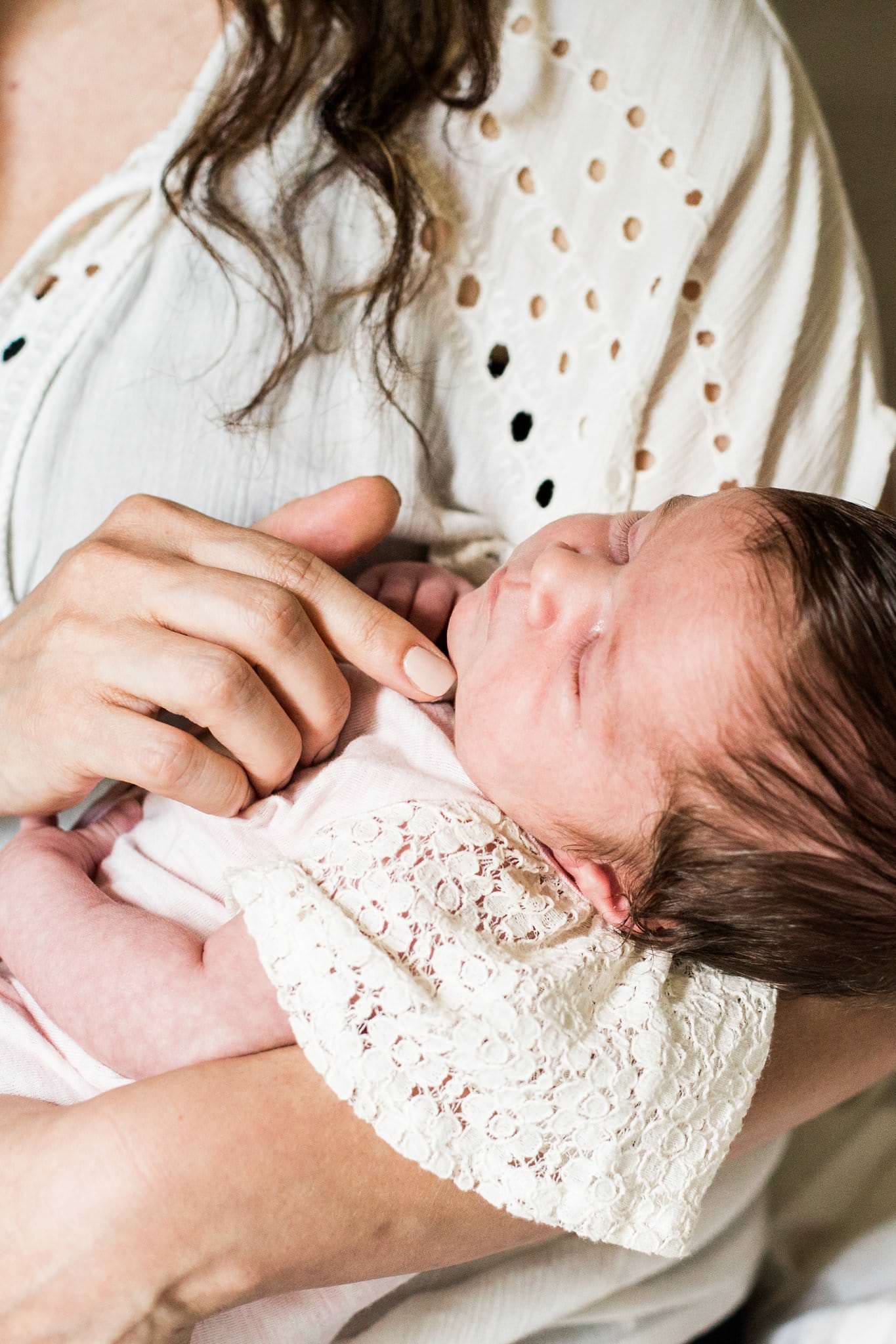 mother holding newborn on bed in home