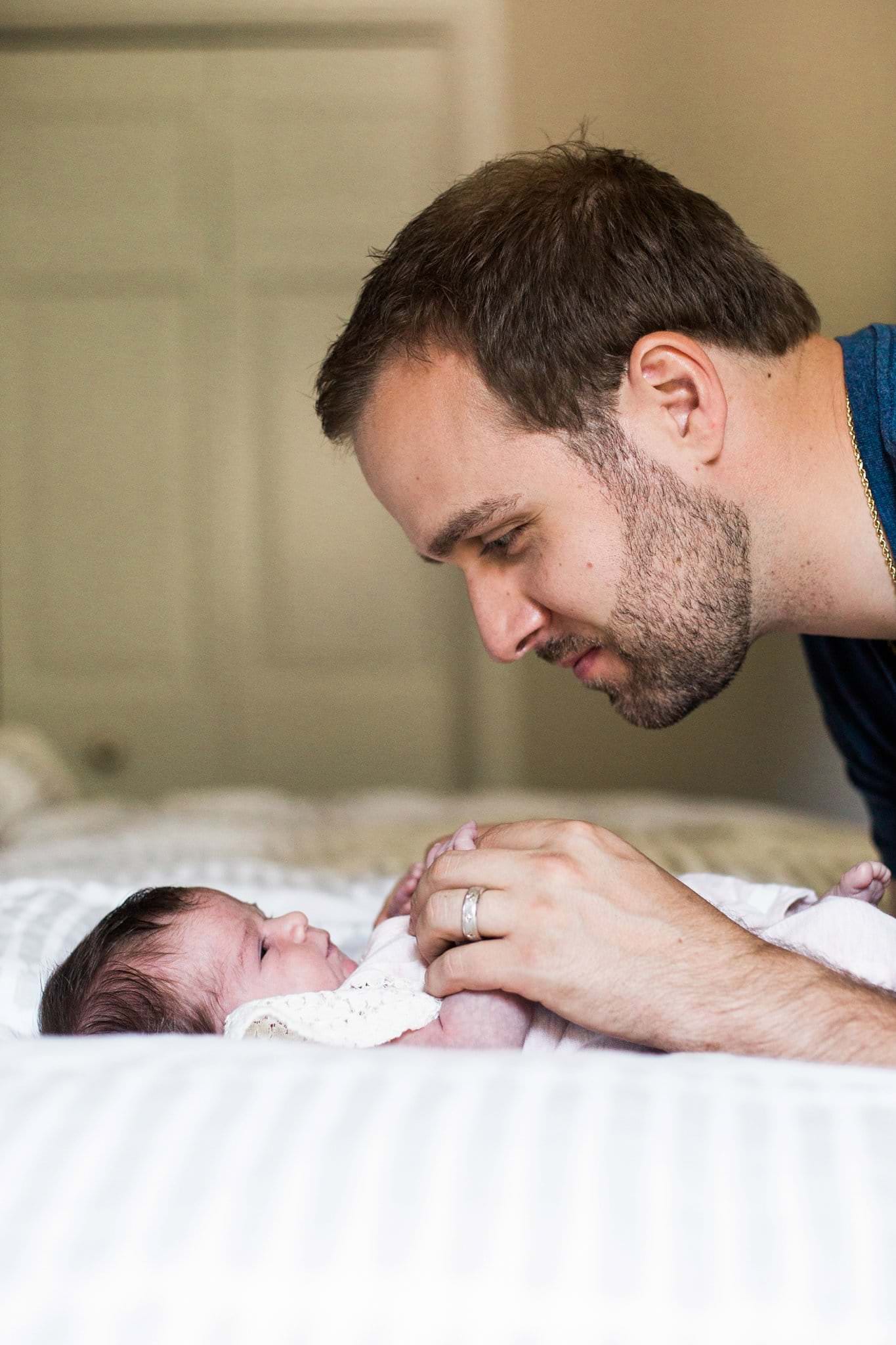 father with newborn on bed in home