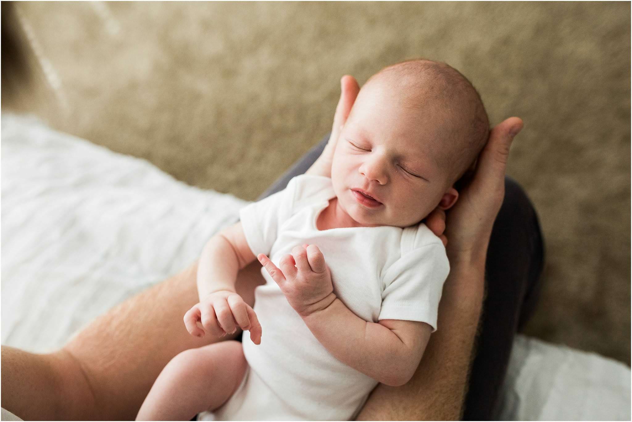 newborn baby boy in white onesie held by father