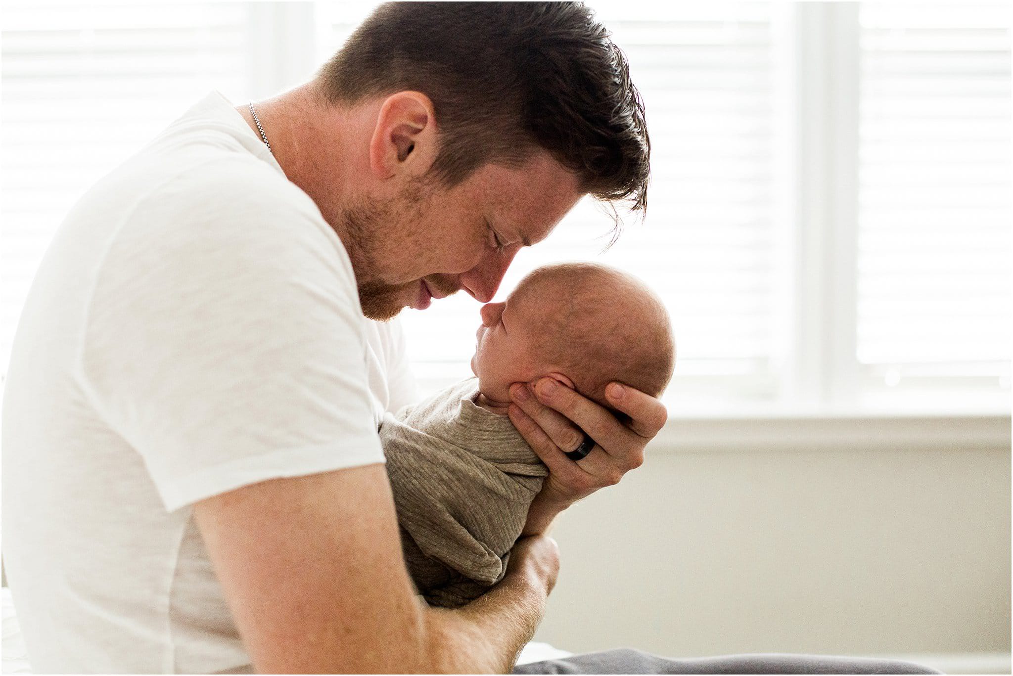 father holding newborn son in bedroom of home