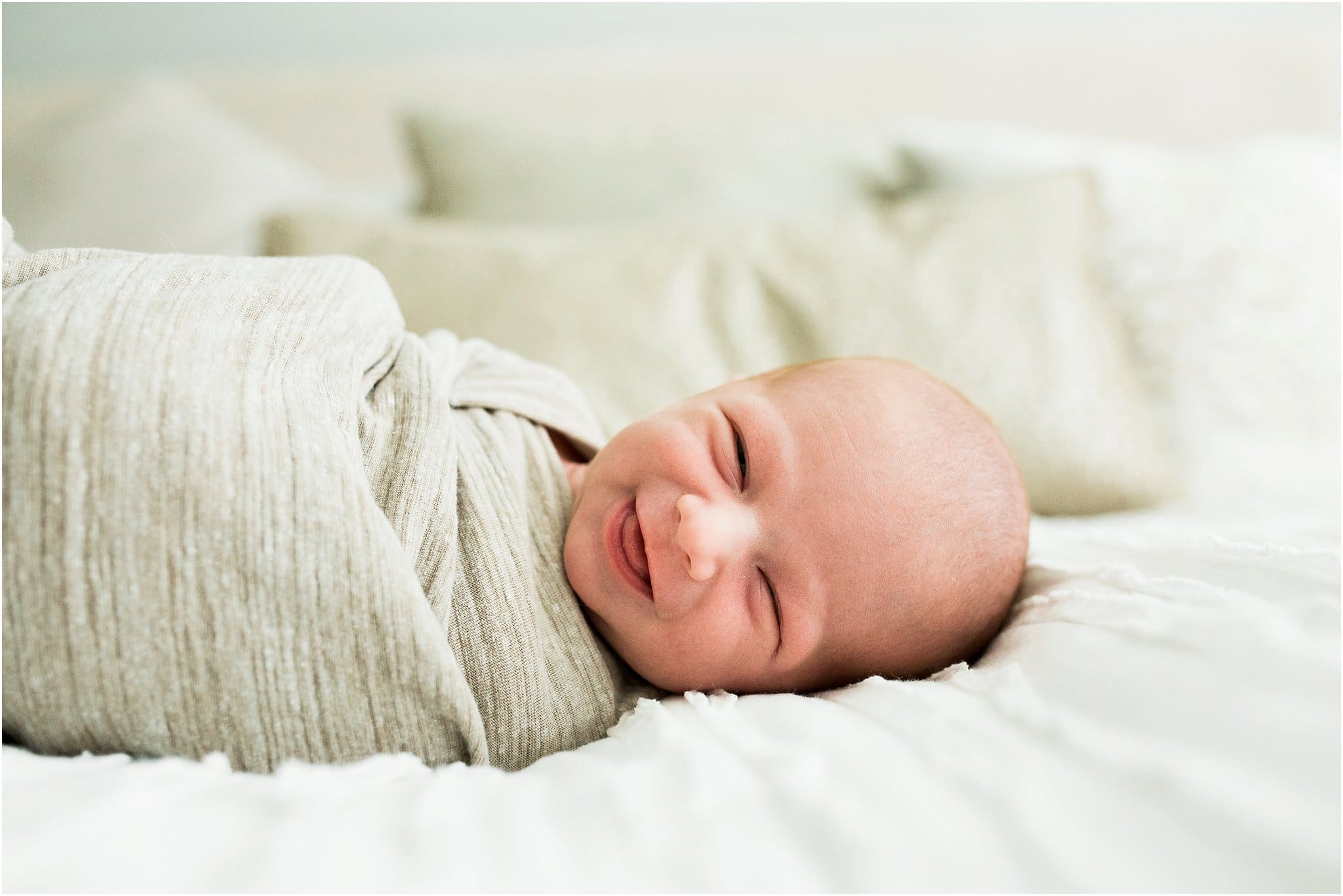smiling newborn swaddled on bed