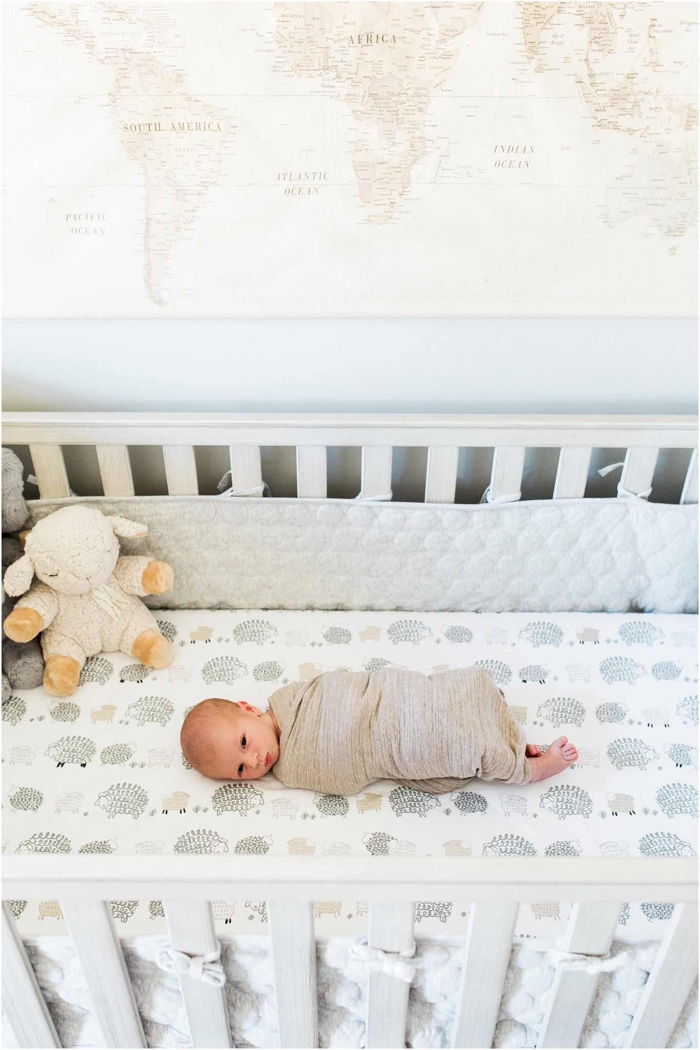 newborn boy in neutral crib with world map decor