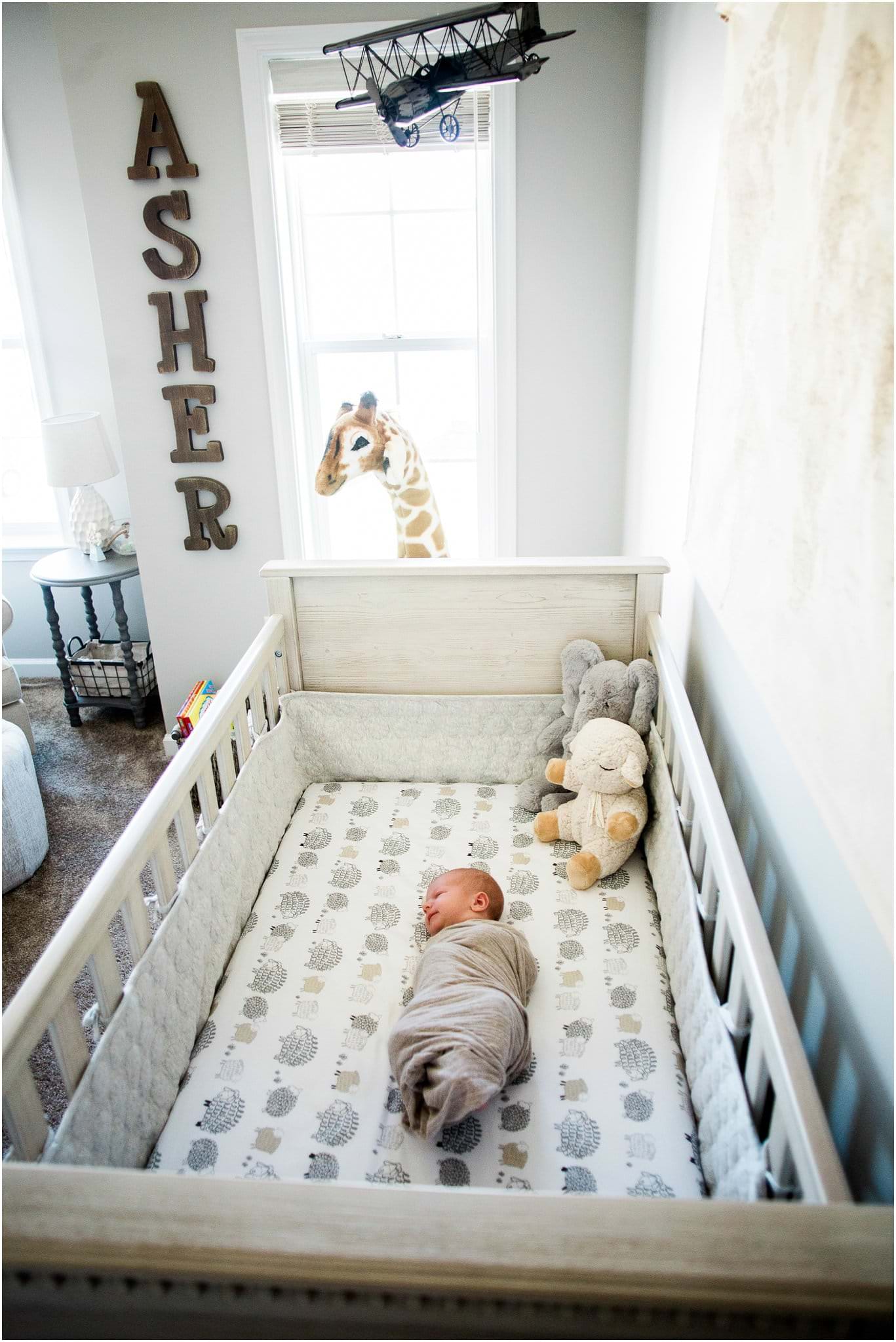 newborn boy in neutral crib with world map decor