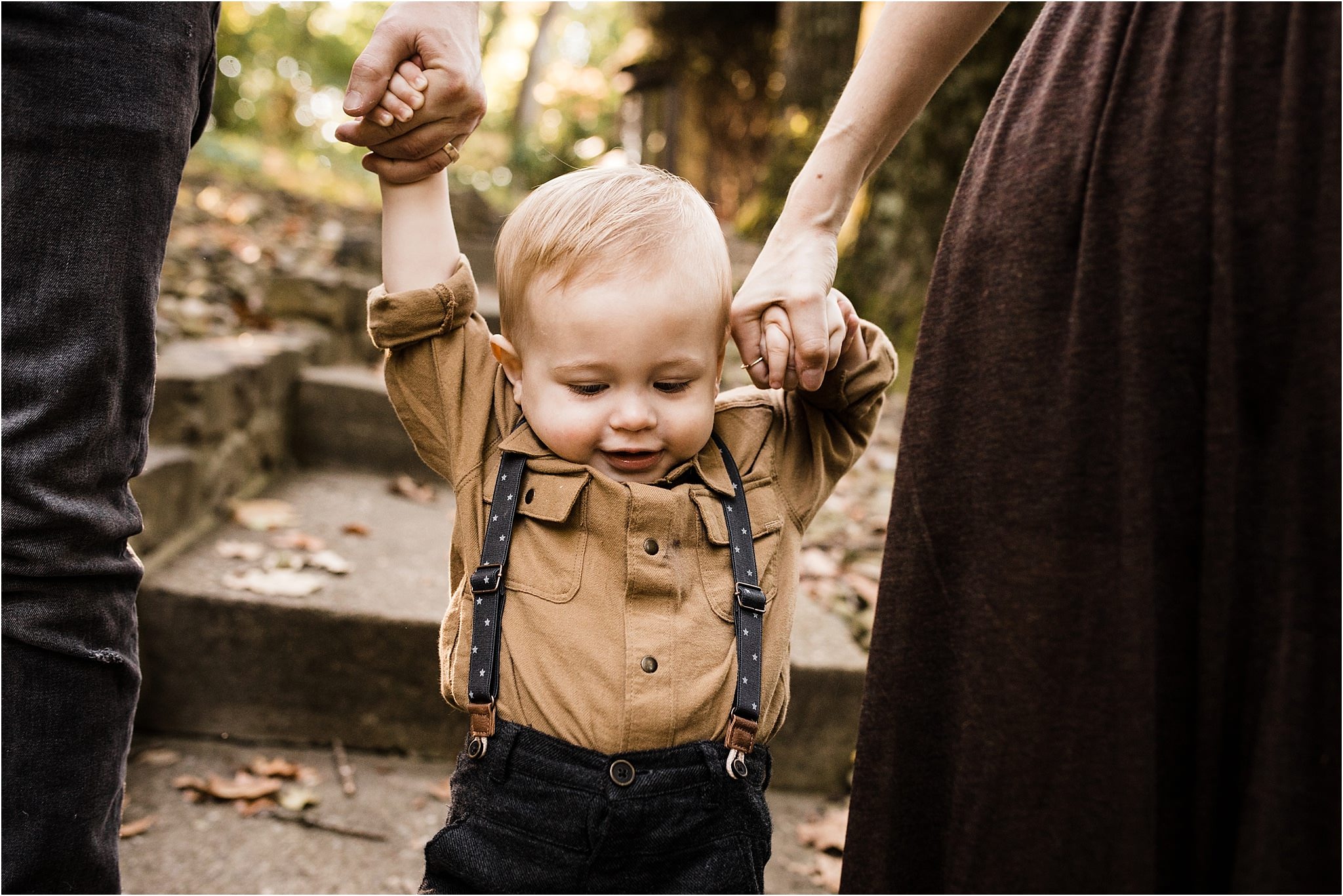 one year old boy walking holding parents hands