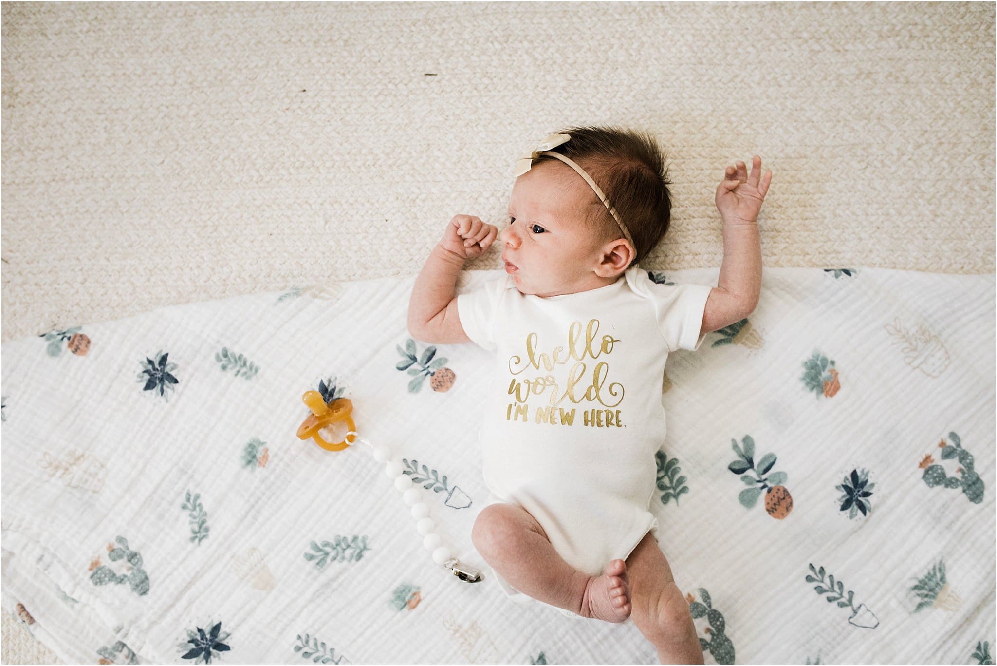 newborn baby girl laying on floral swaddle wearing i'm new here onesie