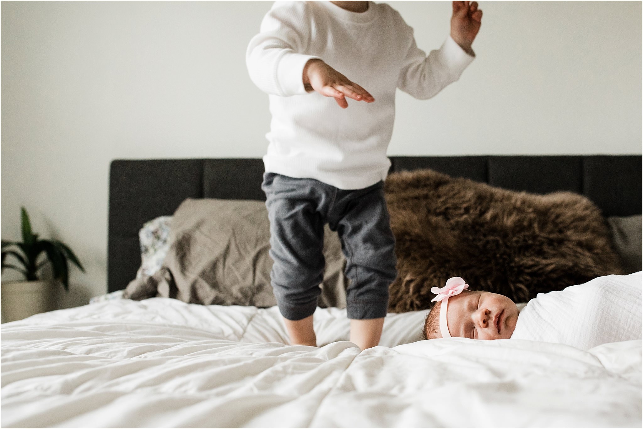 newborn baby sleeping while toddler jumps on bed