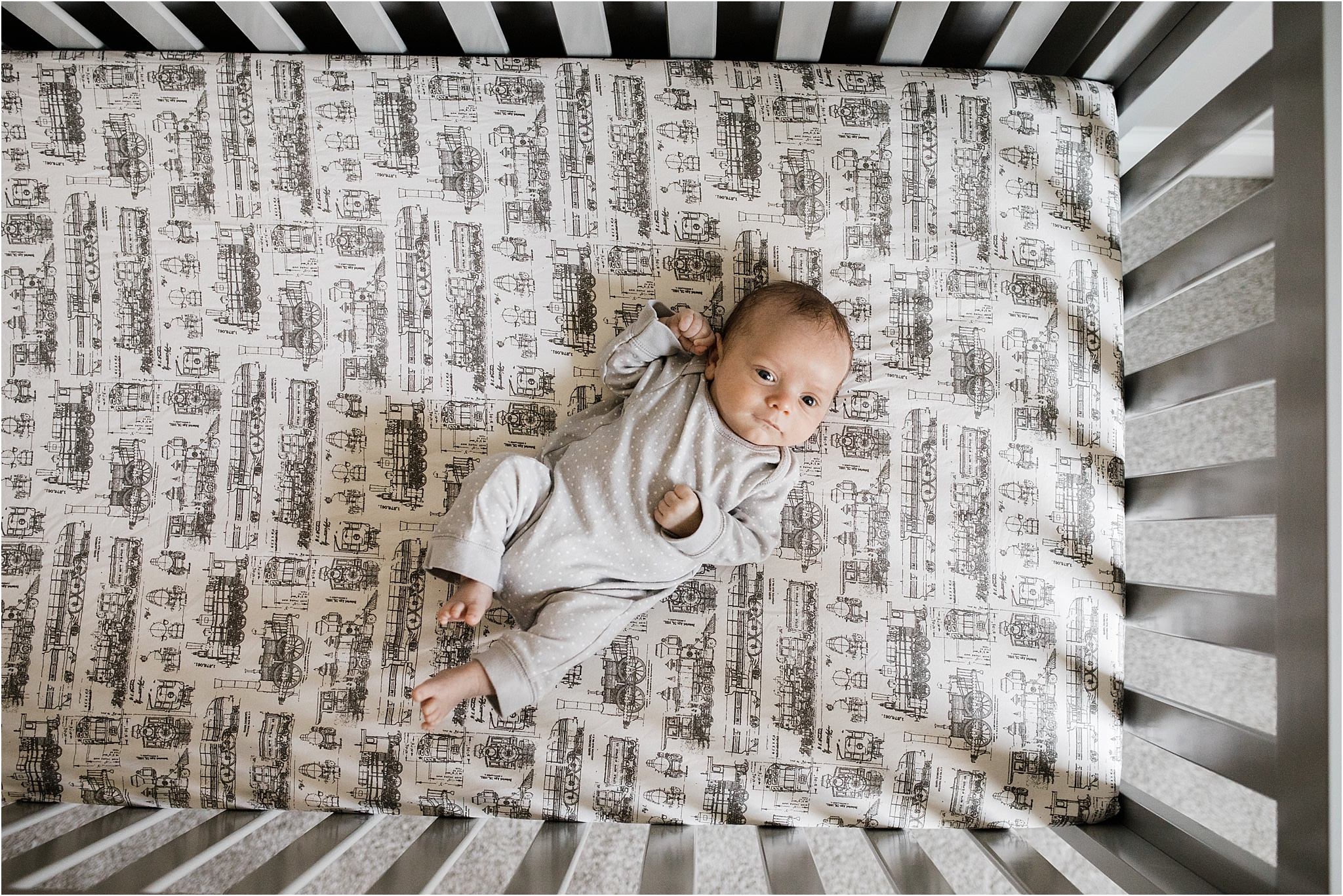 newborn baby boy in crib with train sheets