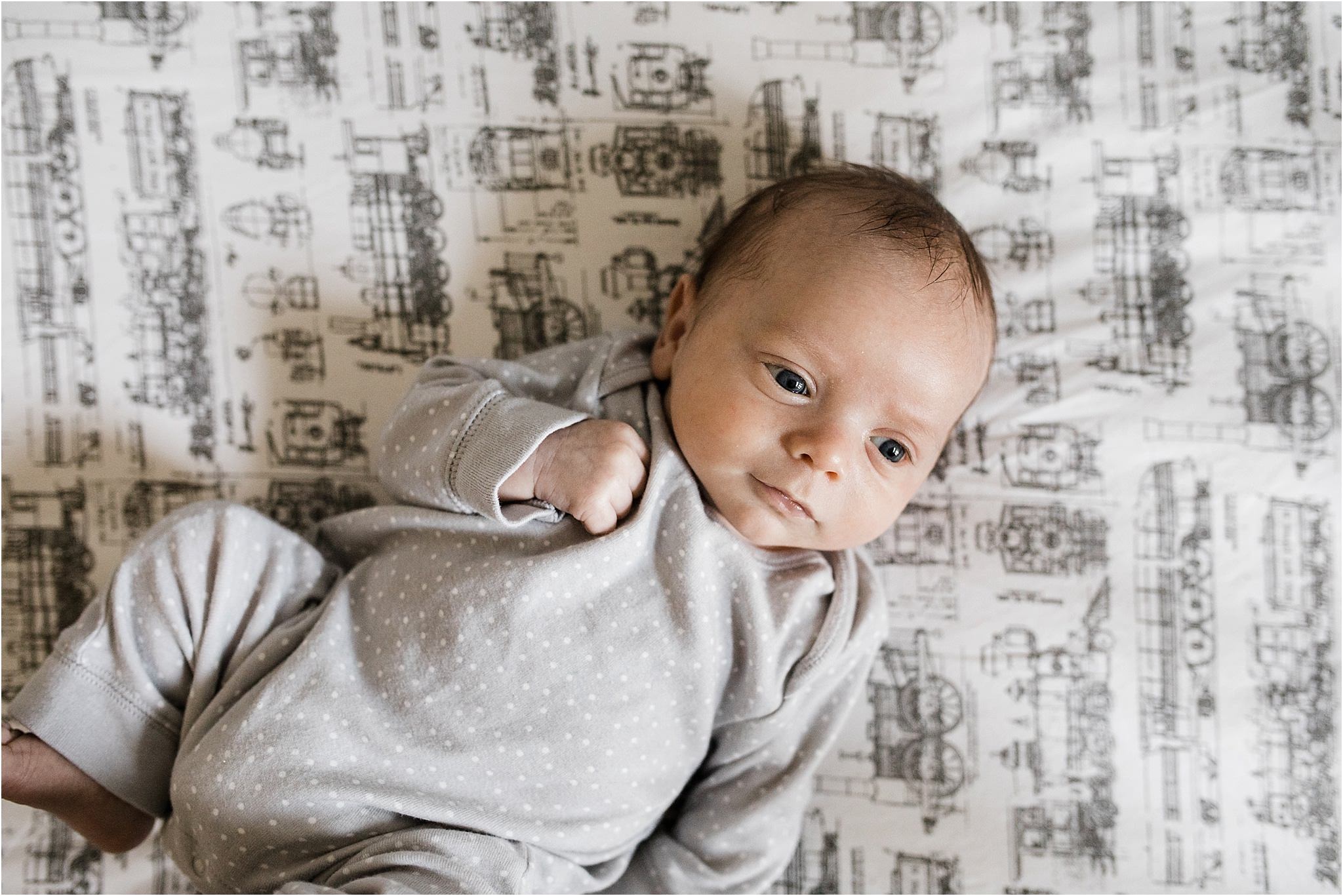 newborn baby boy in crib with train sheets