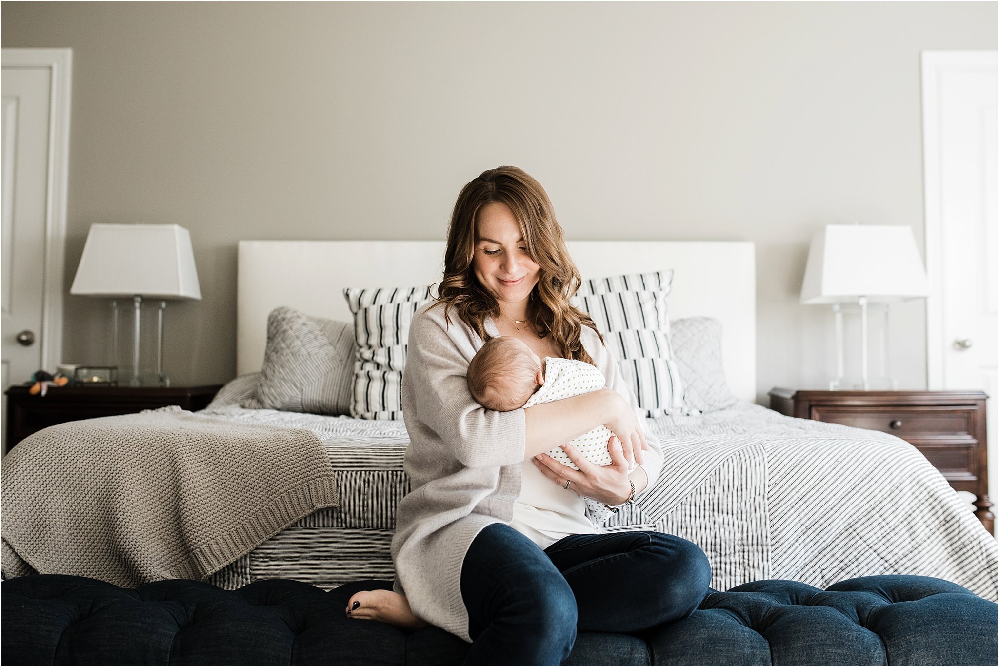 beautiful mother holding and looking at newborn baby in bedroom during home newborn session