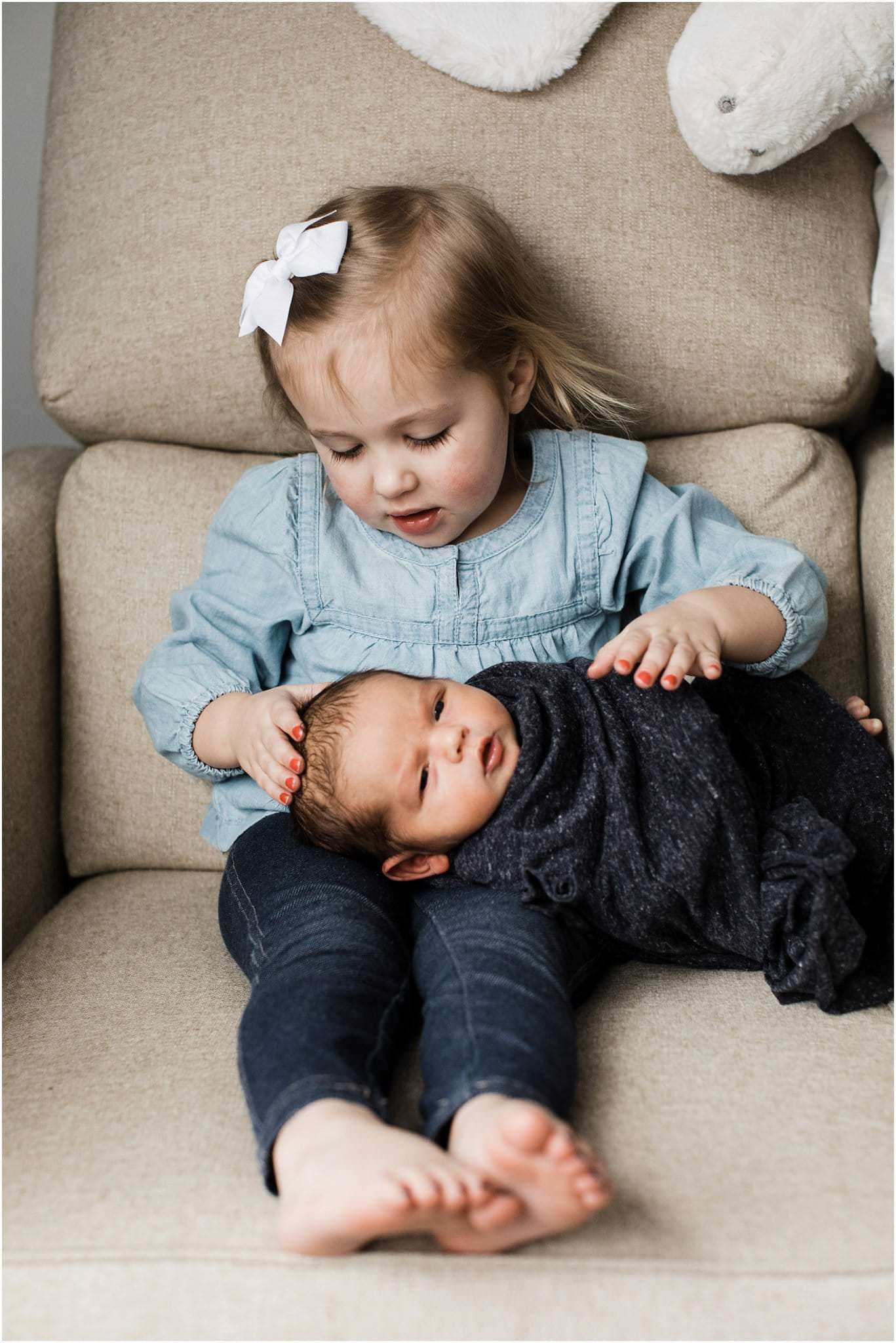big sister with newborn baby brother on chair in nursery