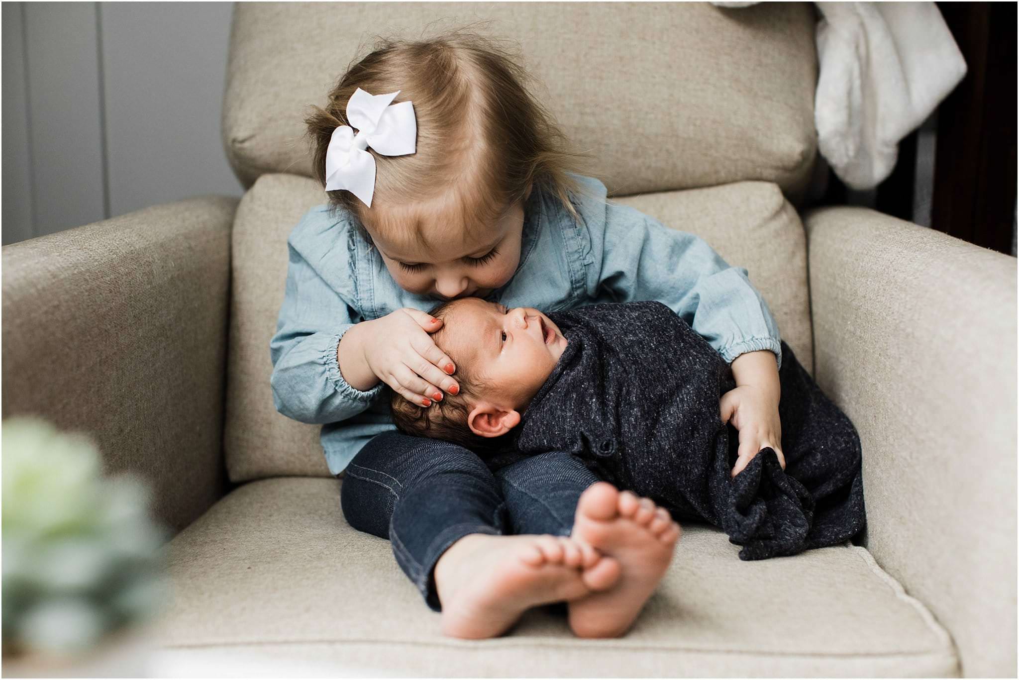 big sister with newborn baby brother on chair in nursery