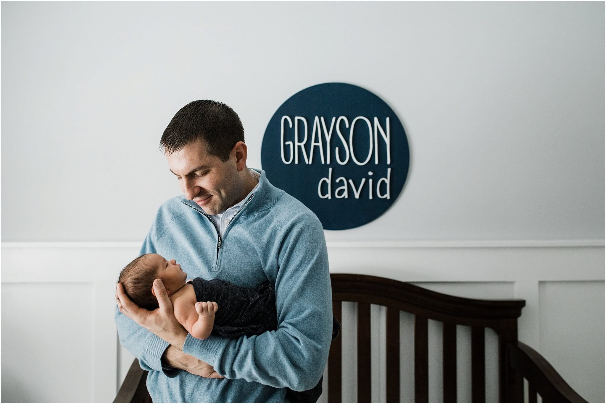 father holding newborn son in nursery