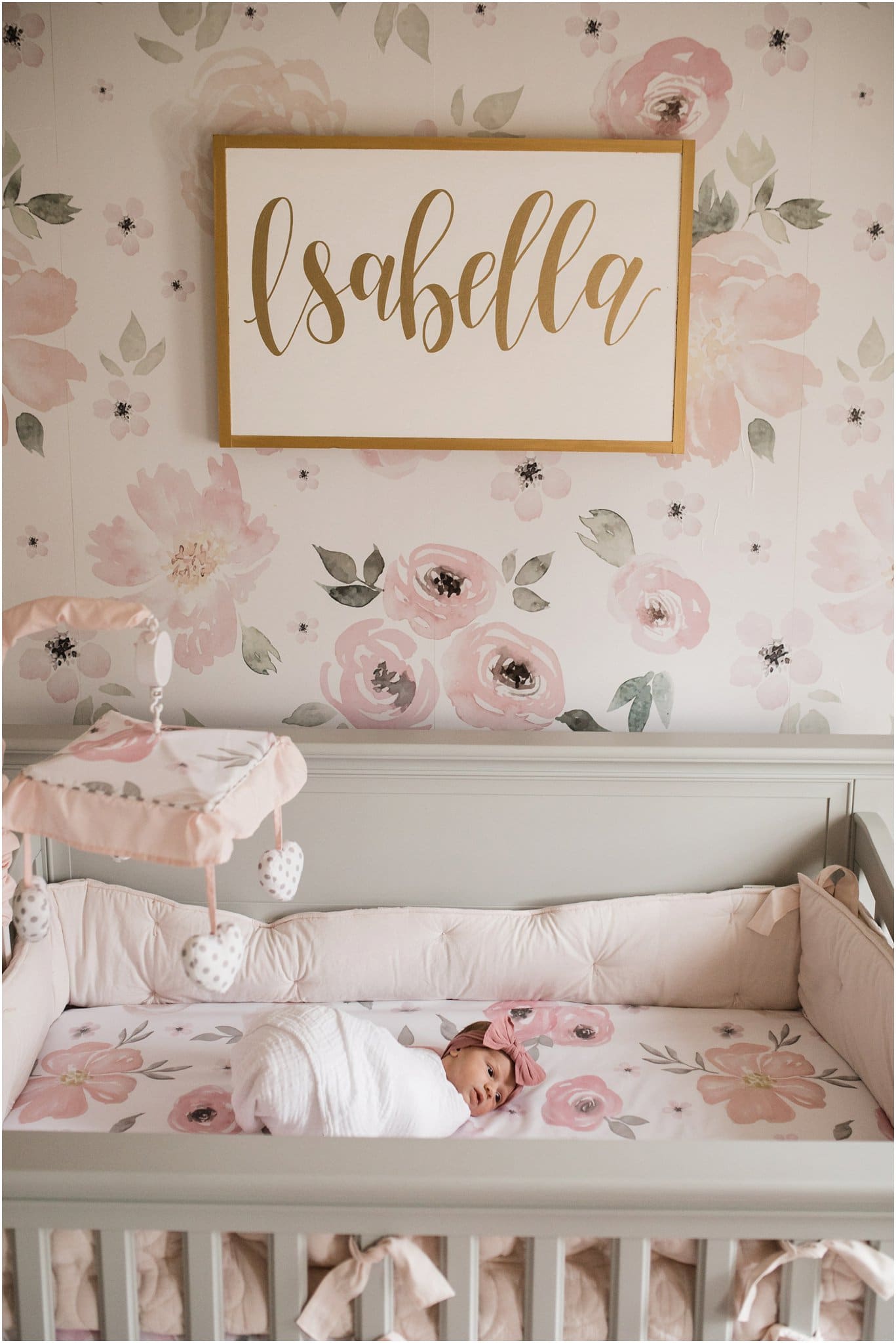 Natural swaddled newborn girl with pink bow and floral crib sheets and wallpaper