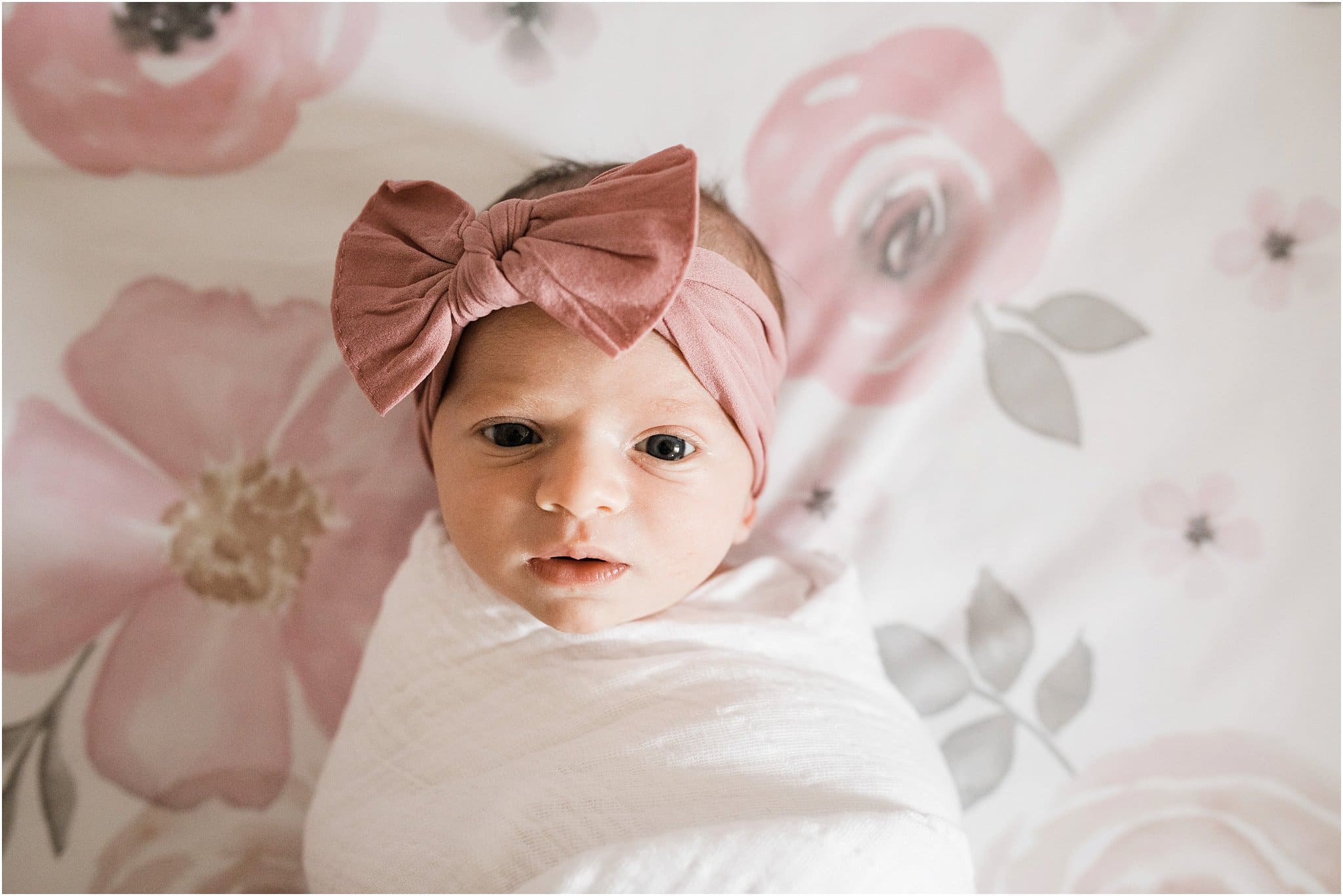 Natural swaddled newborn girl with pink bow and floral crib sheets