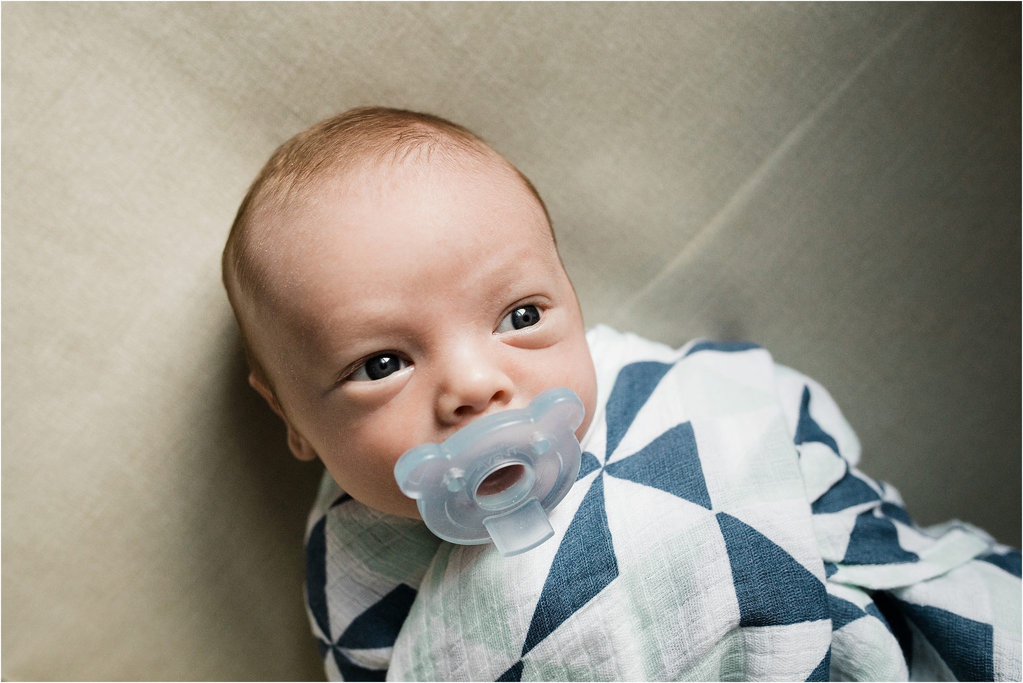 newborn boy with blue pacifier and pattern swaddle