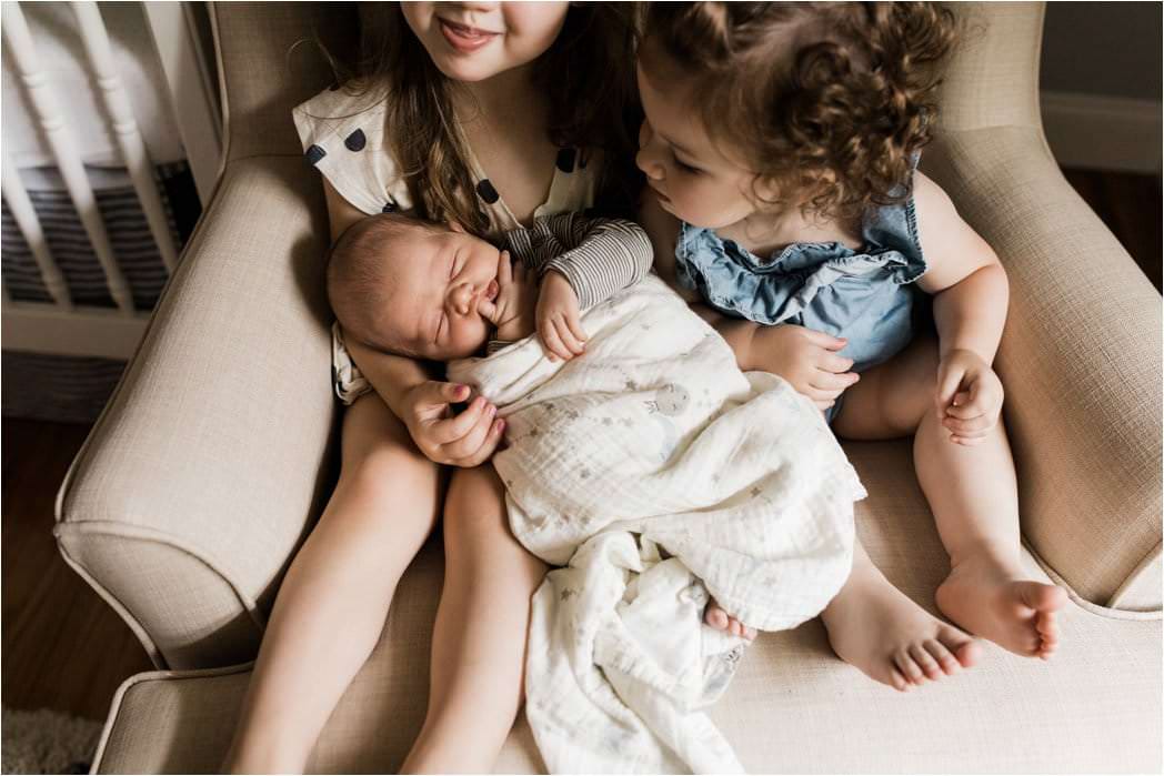 big sisters holding newborn baby bbrother