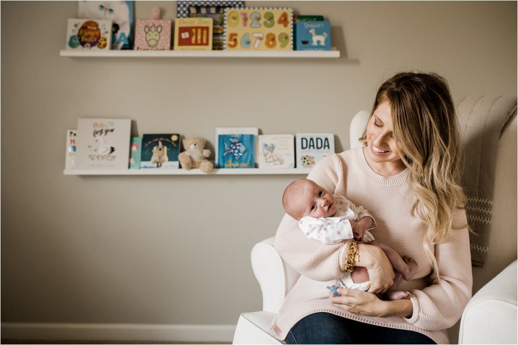 new mom holding newborn baby girl in neutral nursery with book shelves