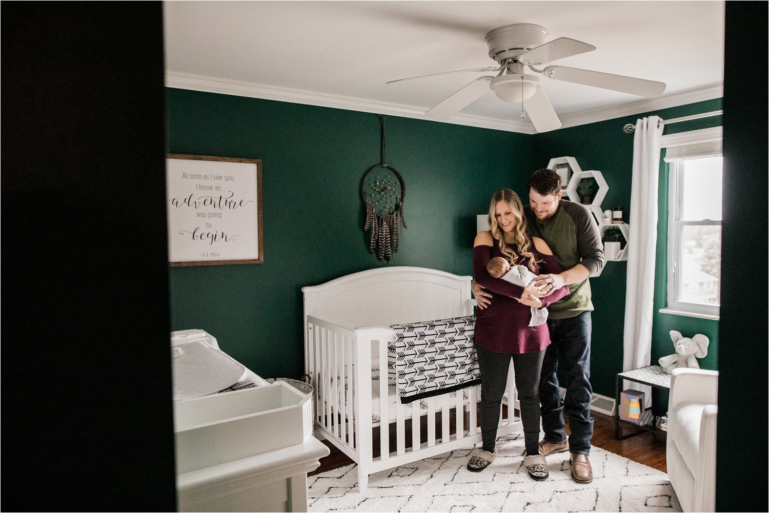 new parents with newborn baby in stylish green nursery with white accents