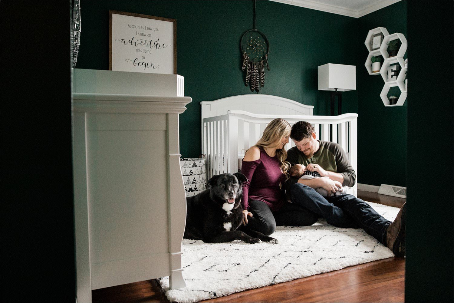 parents hoding newborn with black lab in green and white nursery