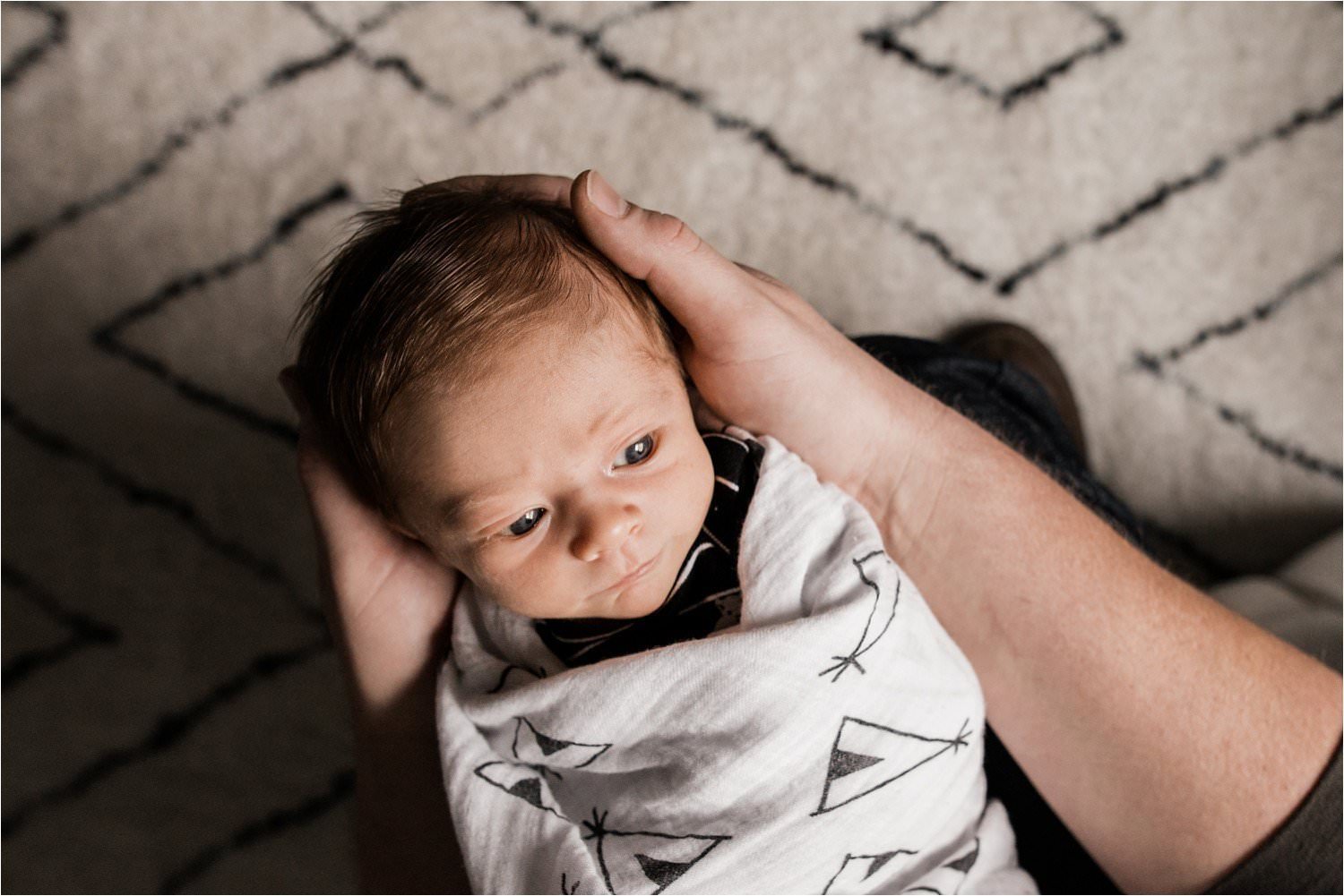 newborn baby boy wrapped in swaddle blanket held in fathers hands