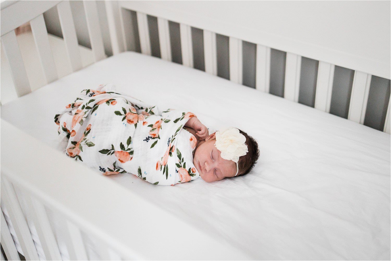 baby in floral swaddle in crib at home