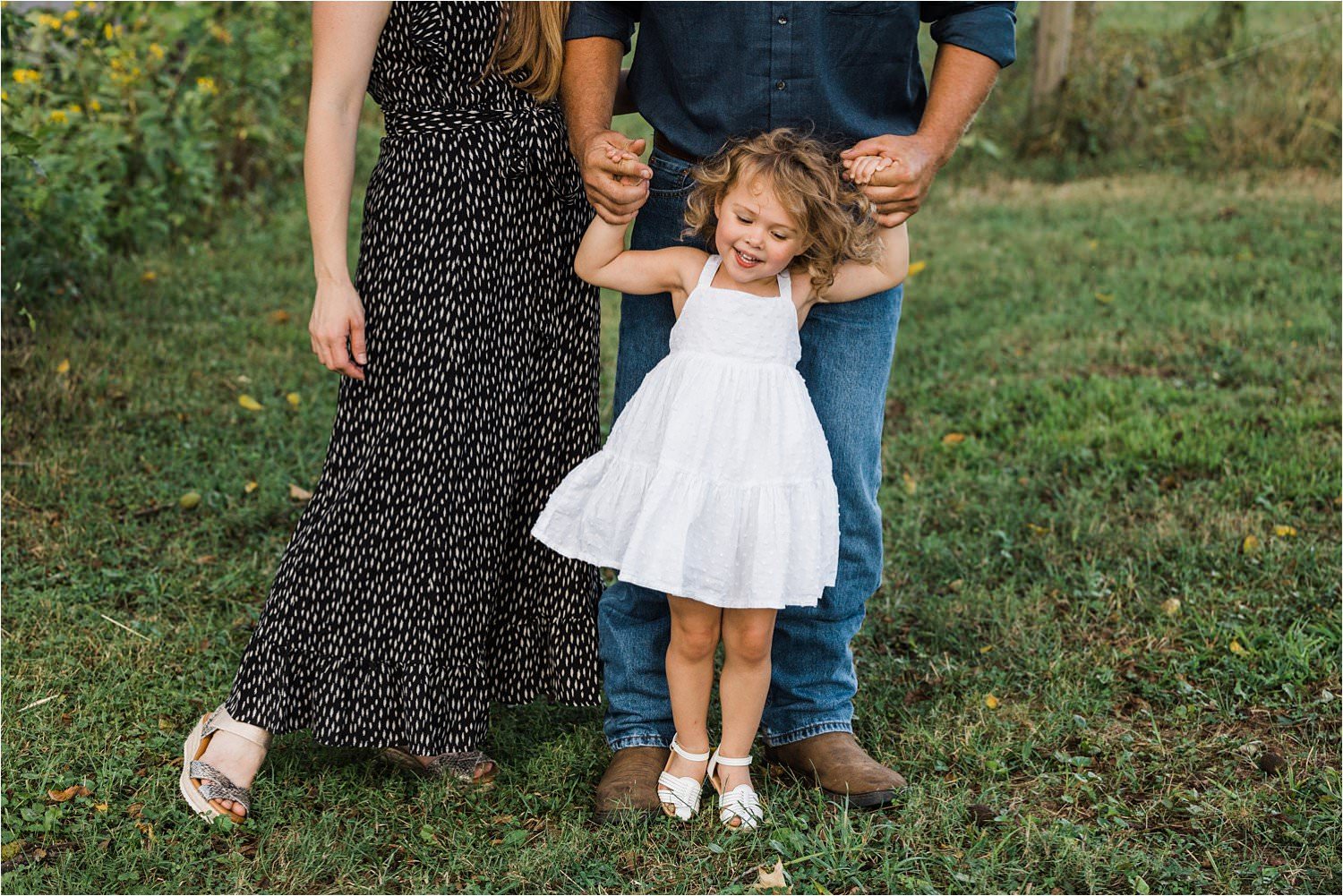 little girl in white dress holding parents hands