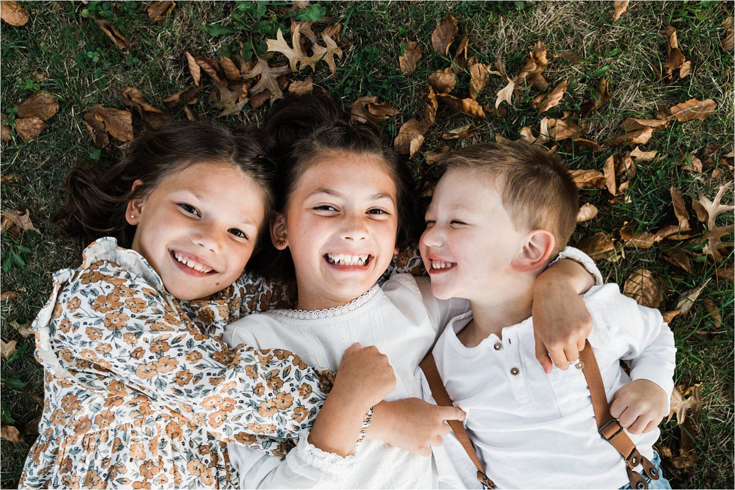 three siblings laying snuggled in the leaves